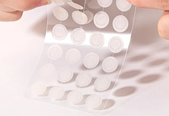 A hand peeling a TKTK hydrocolloid patch from its clear sheet